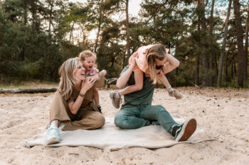 Gezin met 2 jonge dochters zittend op een kleedje in de Loonse en Drunense duinen tijdens een gezinsshoot van Moment Fotografie