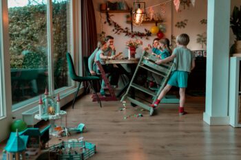 Gezin aan tafel tijdens de lunch, speelgoed ligt op de vloer en jongste zoon staat naast zijn stoel. Een stilleven van een doodnormaal gezin tijdens een day-in-the-life-reportage van Moment Fotografie
