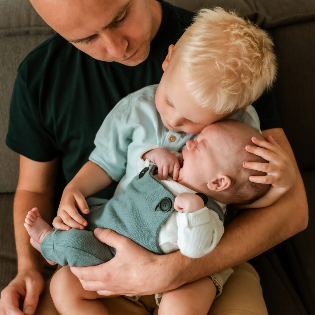 newborn op schoot bij zijn grote broer, die ook weer op schoot zit van zijn vader