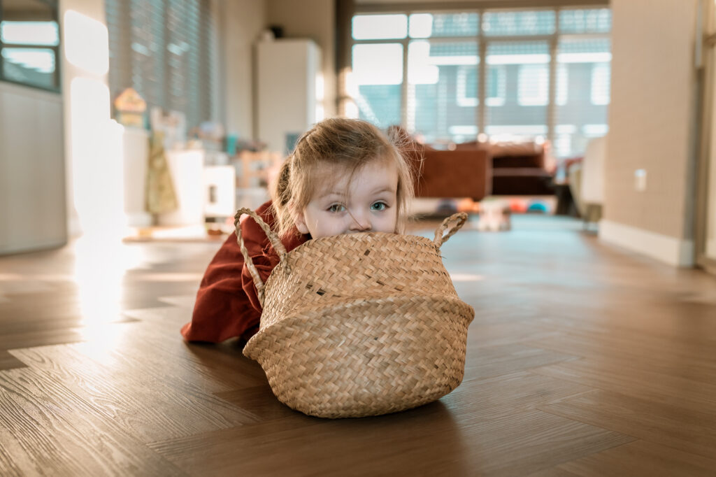 Meisje komt net met haar hoofd boven een rieten speelmand uit