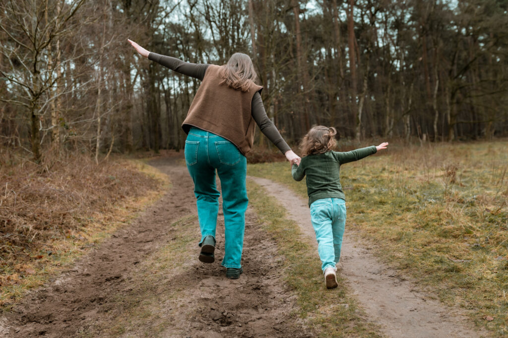 Moeder en dochter rennen hand in hand het bos in tijdens een fotoshoot bij Moment Fotografie